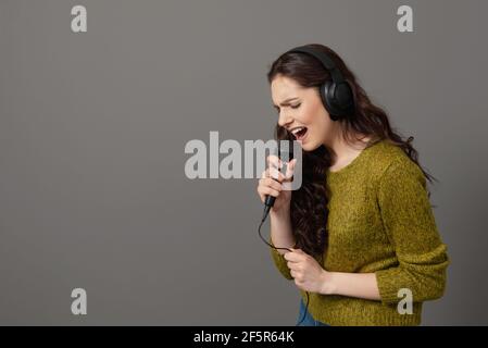 une adolescente chante avec un micro et un casque, isolée sur le gris Banque D'Images