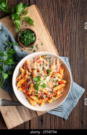 Classique penne all'Arabiata, pâtes épicées à la sauce tomate et Chili, nappées de fromage râpé sur fond de bois rustique Banque D'Images