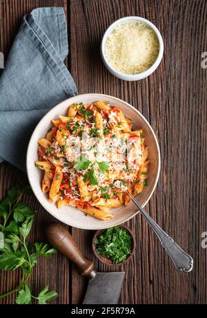 Classique penne all'Arabiata, pâtes épicées à la sauce tomate et Chili, nappées de fromage râpé sur fond de bois rustique Banque D'Images