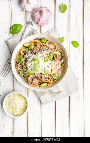 Spaghetti de blé entier sains avec des champignons sautés, de l'ail et des courgettes, nappés de fromage râpé et de feuilles de basilic sur fond de bois rustique Banque D'Images