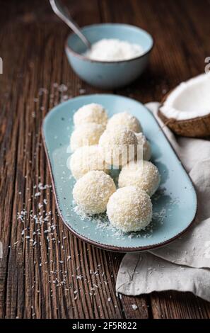 Délicieux bonbons sans cuisson, truffes au chocolat blanc recouvertes de noix de coco râpée sur fond rustique en bois Banque D'Images