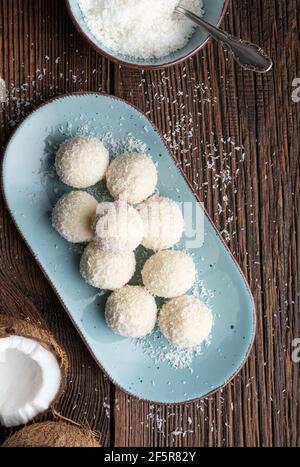 Délicieux bonbons sans cuisson, truffes au chocolat blanc recouvertes de noix de coco râpée sur fond rustique en bois Banque D'Images