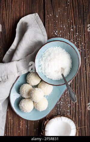 Délicieux bonbons sans cuisson, truffes au chocolat blanc recouvertes de noix de coco râpée sur fond rustique en bois Banque D'Images