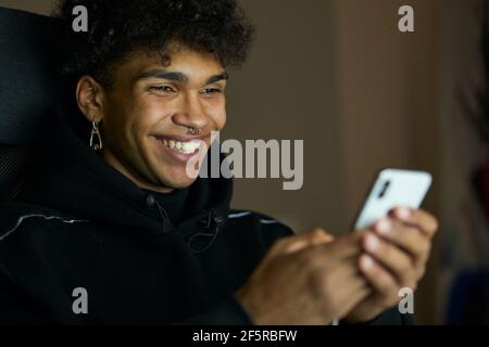 Gros plan de jeune homme souriant qui envoie des SMS, bavarde avec des amis et utilise un smartphone tard dans la nuit à la maison Banque D'Images