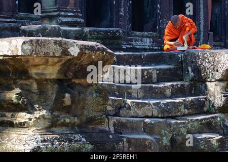 Orange monk. Un moine bouddhiste lit un livre Saint assis hors d'un temple ancien. Banque D'Images