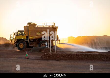 Chariot à eau qui amortit les routes minières poussiéreuses au coucher du soleil à l'ouverture zone d'extraction de la fosse Banque D'Images