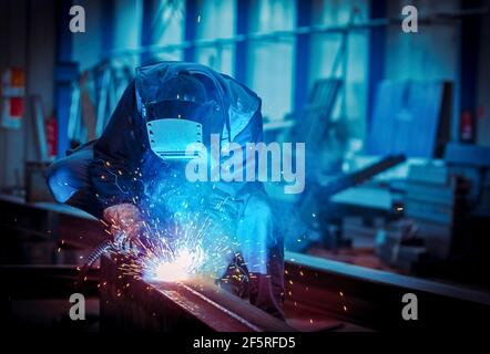 Homme avec un masque de protection et un écran de protection pour les yeux soudant de l'acier industriel poutre Banque D'Images