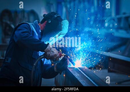 Homme avec un masque de protection et un écran de protection pour les yeux soudant de l'acier industriel poutre Banque D'Images