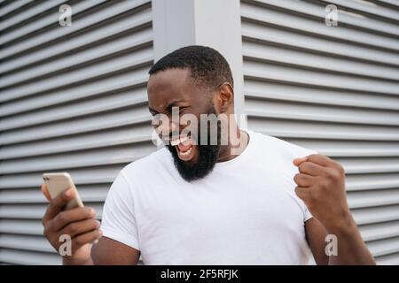 Portrait du gagnant de loterie en ligne surjoyeuse regardant l'écran numérique, célébration succès. Concept de Paris sportifs. Homme excité utilisant le téléphone mobile Banque D'Images