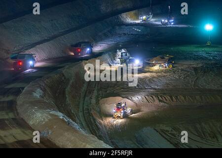 Exploitation minière à ciel ouvert la nuit avec des engins de forage, des camions à benne basculante et des chargeuses fonctionnant sous des projecteurs. Banque D'Images