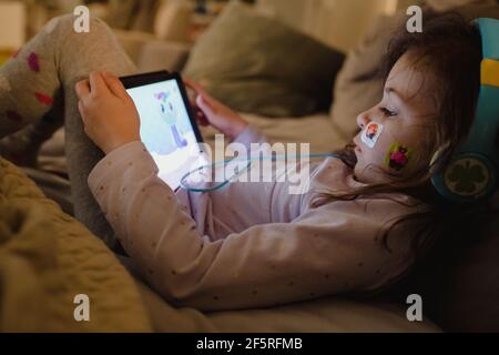 Jeune fille avec bandage sur le visage jouant avec la tablette Banque D'Images