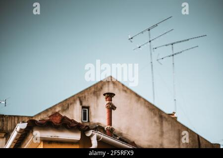 Un toit triangulaire d'une vieille maison avec plusieurs antennes tv, faible profondeur de champ avec un accent sélectif sur la petite cheminée dans le premier plan wrappe Banque D'Images