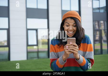 Homme afro-américain enthousiaste utilisant le téléphone mobile, magasiner en ligne. Portrait du gagnant de loterie en ligne surjoyeuse regardant l'écran numérique Banque D'Images