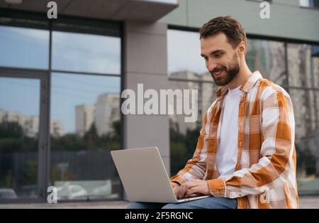 Beau homme d'affaires utilisant ordinateur portable, dactylographie, travail en ligne. Une entreprise prospère. Portrait d'un développeur heureux sur le lieu de travail Banque D'Images