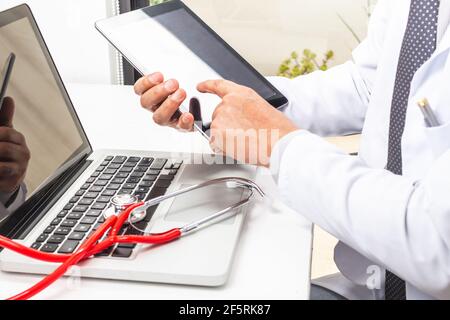 Un médecin dont le visage n'est pas reconnu utilise une tablette avec ses mains pour son travail en médecine avec son ordinateur portable et son stéthoscope dans son bureau. T Banque D'Images