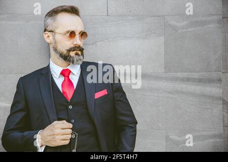 Beau modèle latin à barbe avec costume et lunettes de soleil portrait debout Banque D'Images
