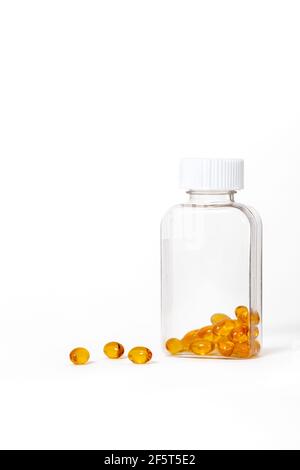 Capsules d'huile de poisson de couleur jaune dans une bouteille en verre sur fond blanc. Banque D'Images