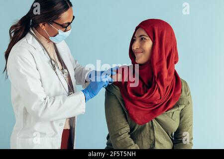 Médecin portant un masque facial et des gants de protection donnant le vaccin à une femme musulmane. Une femme présente dans le hijab et reçoit le vaccin. Banque D'Images