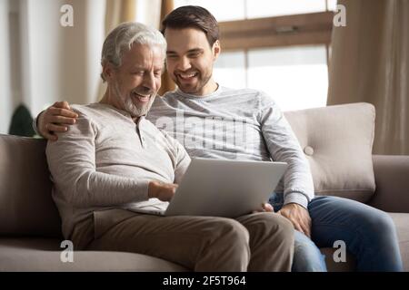 Un père et un fils adultes heureux utilisent un ordinateur portable à la maison Banque D'Images