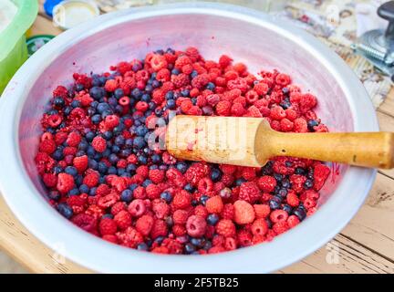 Framboises et groseilles à maquereau dans un bol avec un poussoir, faisant de la confiture maison Banque D'Images