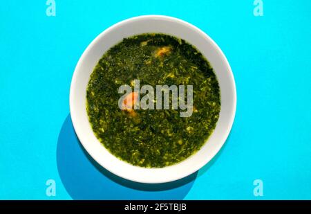 Célèbre cuisine arabe traditionnelle. Soupe Molokhia aux crevettes sur fond bleu. Flat lay, vue de dessus. Moroheiya, Mulukhiya Banque D'Images