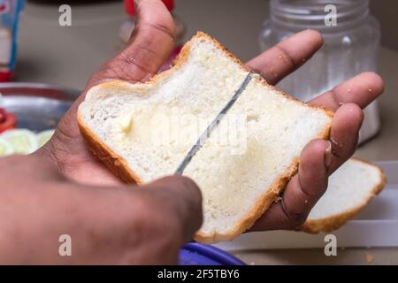 mains appliquant du beurre sur du pain blanc avec un couteau à beurre Banque D'Images