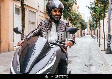 Motard ethnique brutal dans un casque conduisant une moto contemporaine pendant vue sur la ville Banque D'Images