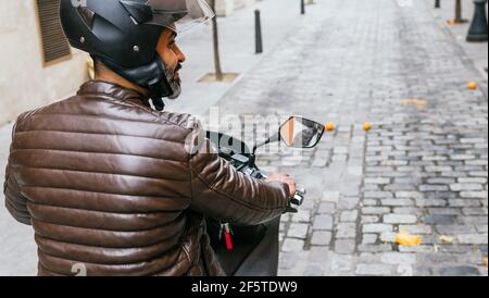 Vue arrière de la violente ethnie motard masculin dans la conduite de casque moto contemporaine tout en regardant de manière en ville Banque D'Images