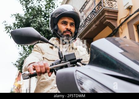De dessous de la violente ethnie motard masculin dans la conduite de casque moto contemporaine avec vue sur la ville Banque D'Images