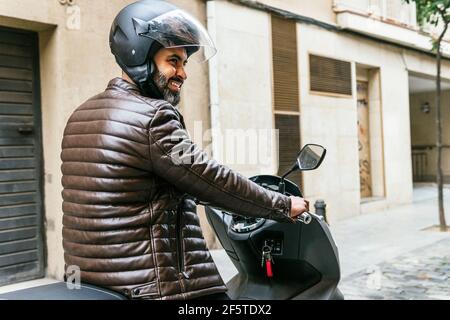 Vue latérale d'un cycliste ethnique brutal lors de la conduite avec un casque moto contemporaine tout en regardant de manière en ville Banque D'Images