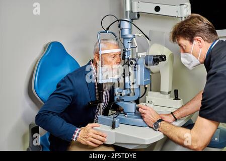 Vue latérale de l'ophtalmologiste professionnel à l'aide d'une lampe à fente et d'une vérification vue d'un patient mâle âgé Banque D'Images