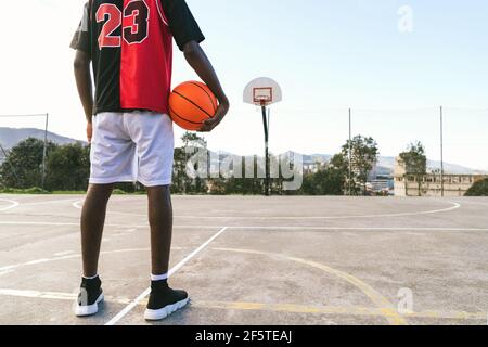 Vue arrière courte d'un joueur de streetball afro-américain méconnaissable en uniforme debout avec ballon sur le terrain de basket-ball Banque D'Images