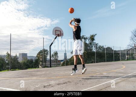 Vue latérale d'un joueur de streetball masculin qui joue au slam dunk au moment de sauter au-dessus du terrain de jeu et de marquer le basket-ball cerceau Banque D'Images