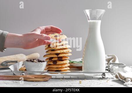 Crop anonyme femme de maison empilant délicieux biscuits faits maison avec des chips de chocolat sur plateau avec un pot de lait frais dans la cuisine Banque D'Images
