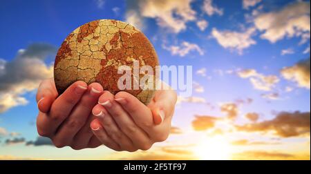 Planète terre parchée entre les mains avec le ciel de coucher de soleil à l'arrière-plan. Réchauffement de la planète ou changement climatique concept. Problèmes environnementaux. Banque D'Images