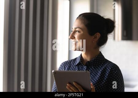 Gros plan femme indienne souriante rêveuse tenant une tablette, planifiant Banque D'Images