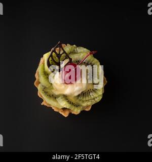 Gâteau de dessert aux fruits avec cerises, feuille de shecolade, quartiers de kiwis et crème aux protéines, sur fond noir isolé Banque D'Images