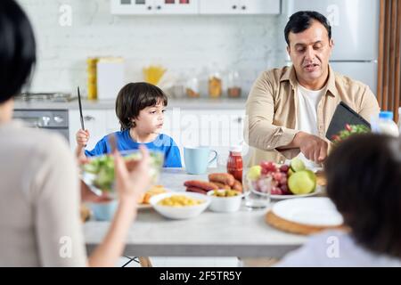 Père d'âge moyen discutant avec son enfant tout en prenant le petit déjeuner le matin. Famille latine en train de savourer un repas ensemble, assis à la table dans la cuisine Banque D'Images