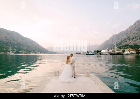 La mariée dans une couronne et un marié embrassent sur le jetée près de la vieille ville de Kotor dans la baie De Kotor Banque D'Images
