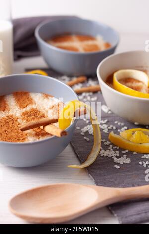 concept d'une durée de vie de plusieurs bols de riz au pudding avec du riz dispersé sur la table, des tranches de citron, une cuillère en bois et des bâtons de cannelle Banque D'Images