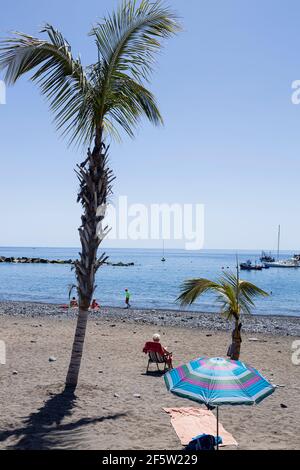 Peu de personnes sur la plage par des palmiers et un parasol et une serviette sur le sable à Playa San Juan, Tenerife, îles Canaries, Espagne Banque D'Images