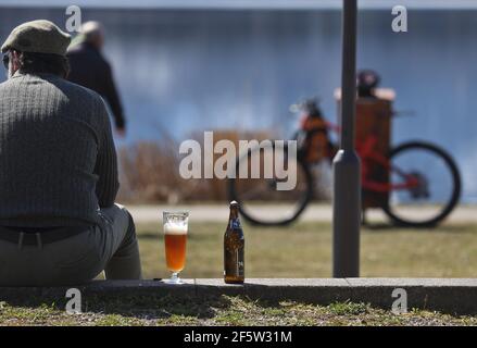 28 mars 2021, Bavière, Füssen: Une journée de tripper se trouve sur les rives de l'Hopfensee avec un verre de bière au soleil. Photo : Karl-Josef Hildenbrand/dpa Banque D'Images