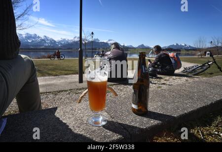 28 mars 2021, Bavière, Füssen: Une journée de tripper se trouve sur les rives de l'Hopfensee avec un verre de bière au soleil. Photo : Karl-Josef Hildenbrand/dpa Banque D'Images