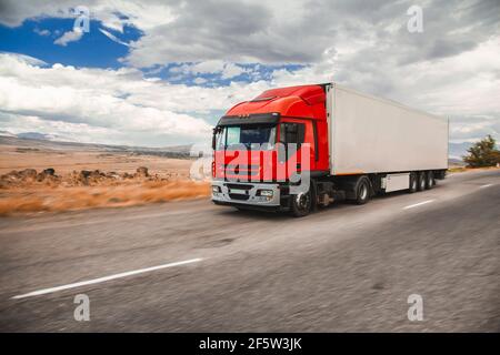 Camion rouge floue sur route asphaltée sur fond de ciel bleu nuageux Banque D'Images