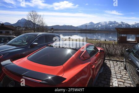 28 mars 2021, Bavière, Füssen: Des excursions s'assoient sur les rives de l'Hopfensee, derrière des voitures garées. De nombreuses personnes ont été attirées par le Hopfensee au soleil. Quelques-uns d'entre eux sont venus en voiture. Photo : Karl-Josef Hildenbrand/dpa Banque D'Images