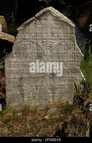 Cette ancienne tête est parmi environ 12,000 monuments qui se trouvent à proximité des murs de l'ancien cimetière juif dans le quartier juif ou Josefov à Prague, capitale de la République tchèque / Tchéquie. Les mémoriaux visibles cachent probablement environ 100,000 000 inhumations dans jusqu'à 12 couches souterraines. Le cimetière a été utilisé pendant près de 350 ans et, lorsque les couches ont été montées, quelques pierres tombales anciennes ont été soulevées à la nouvelle surface. Les premiers portent uniquement des inscriptions hébraïques, mais les exemples suivants comportent des symboles qui font allusion au nom, au caractère ou à la profession du défunt. Banque D'Images