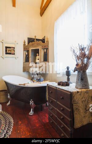 Baignoire et commode à pied à griffe noire dans la salle de bains principale avec planchers de planches larges et colorées rougeâtres à l'intérieur d'un vieux vers 1790 Maison de style cottage Canadiana Banque D'Images