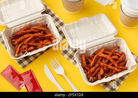 Boîtes à lunch avec frites patate douce, boisson et sauce sur table jaune. Plan d'appartement vue du dessus concept de livraison de nourriture Banque D'Images