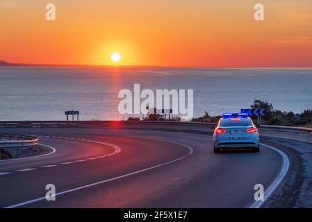 Patrouille de police en charge de surveiller la circulation sur les routes, conduite sur une route de montagne avec la mer et le soleil à l'horizon. Banque D'Images