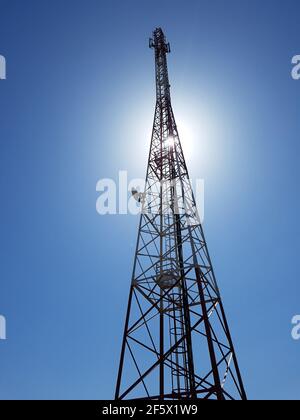 vue verticale à faible angle de la tour de réseau cellulaire ou mobile contre le soleil dans le ciel bleu. Banque D'Images